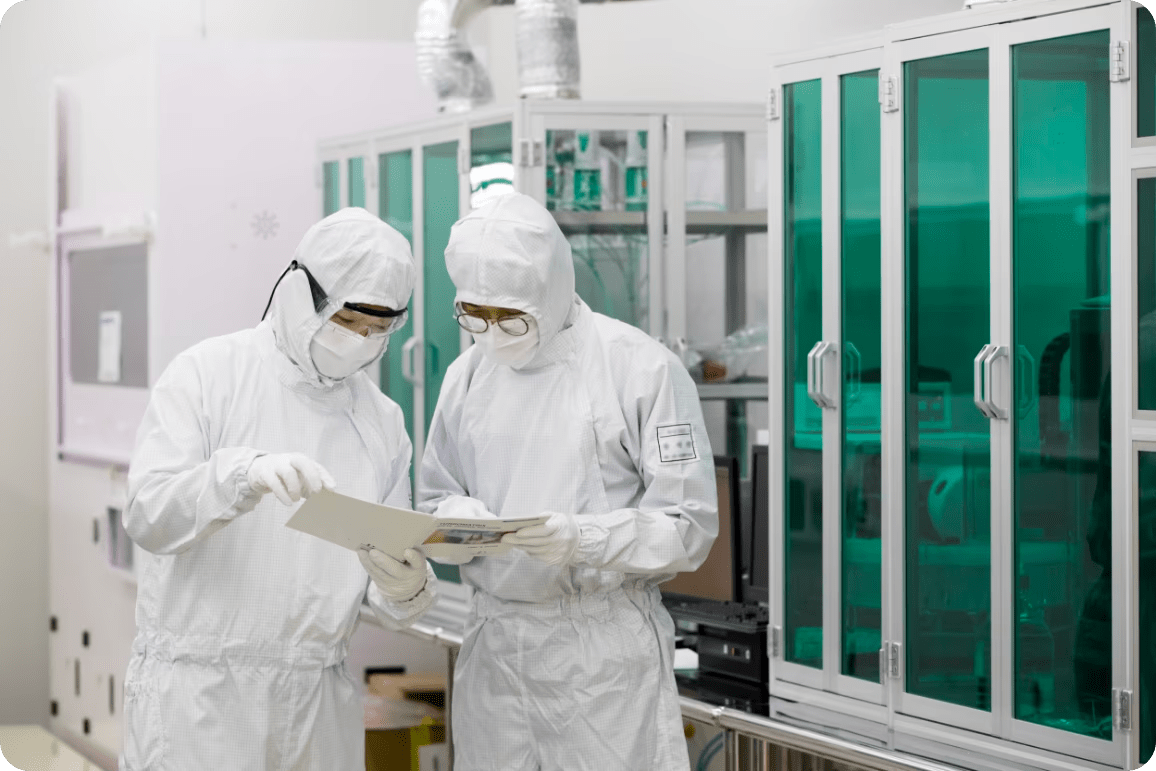 Two engineers wearing protective suits review documents in a clean room