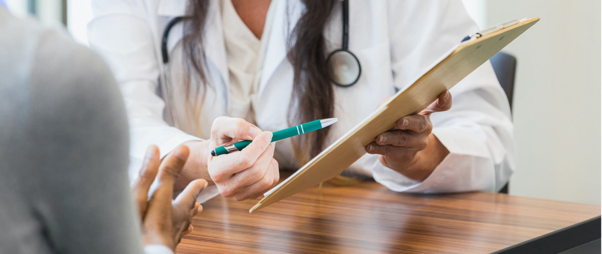 A doctor is pointing a clipboard towards a patient and explaining it.